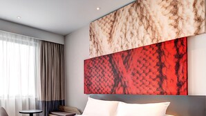 Een moderne hotelkamer met een groot bed, een klein rond tafeltje, een stoel en een nachtkastje met een lamp.