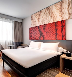Une chambre d’hôtel moderne avec un grand lit, une petite table ronde, une chaise et une table de chevet avec une lampe.