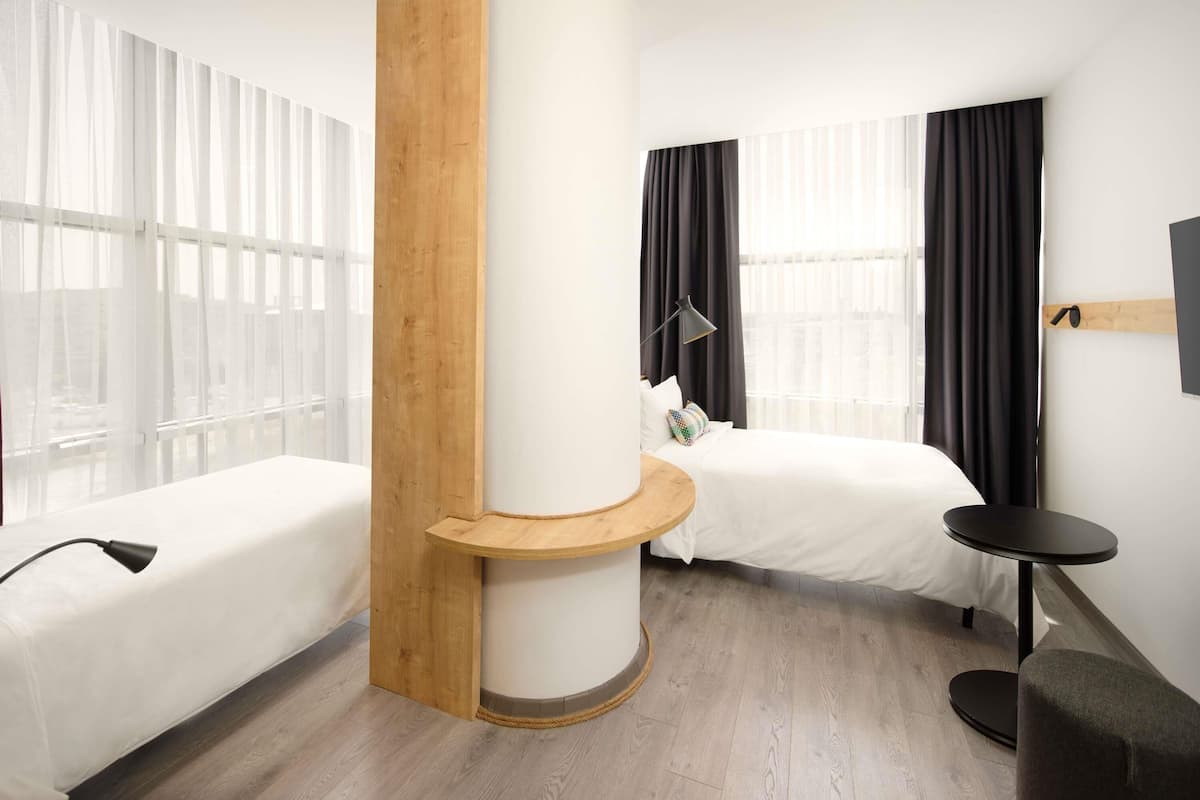 A hotel room with two beds, a wooden accent wall, a small round table, and a lamp.