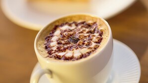 A cup of coffee with a frothy top on a saucer, placed on a wooden table. - Ibis Istanbul Airport (Arnavutköy)
