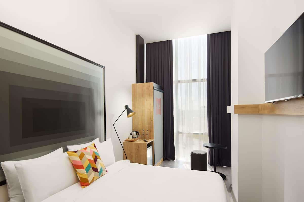 A modern hotel room with a large bed, a desk, a TV, and a window with curtains.
