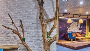 A room with a brick wall, a wooden tree structure, and a stage with chairs and a backdrop. - Ibis Istanbul Airport (Arnavutköy)