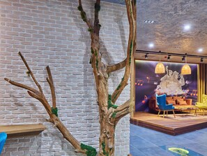 A room with a brick wall, a wooden tree structure, and a stage with chairs and a backdrop. - Ibis Istanbul Airport (Arnavutköy)