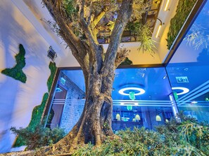 A large indoor tree with a modern interior design, including a brick wall and glass ceiling. - Ibis Istanbul Airport (Arnavutköy)