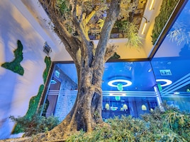 Un gran árbol en el interior, con un diseño moderno que incluye una pared de ladrillo y un techo de cristal.