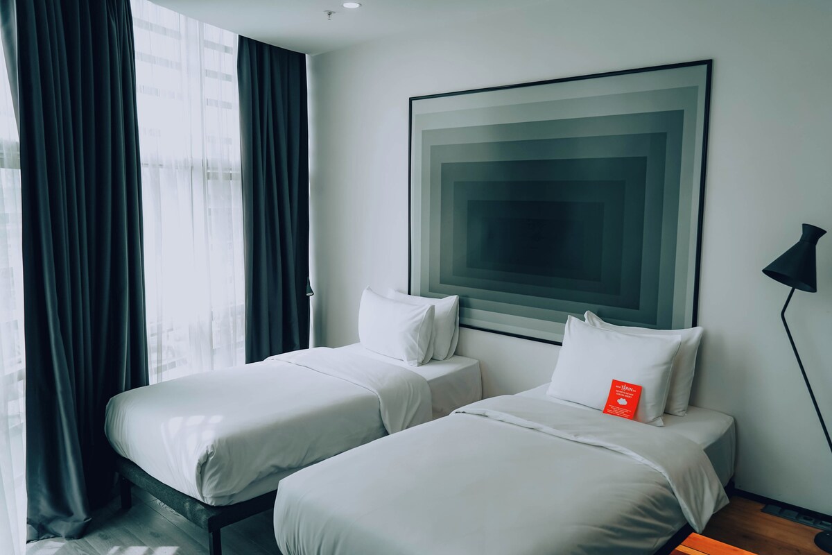 A hotel room with two beds, a large abstract painting on the wall, and a black floor lamp.
