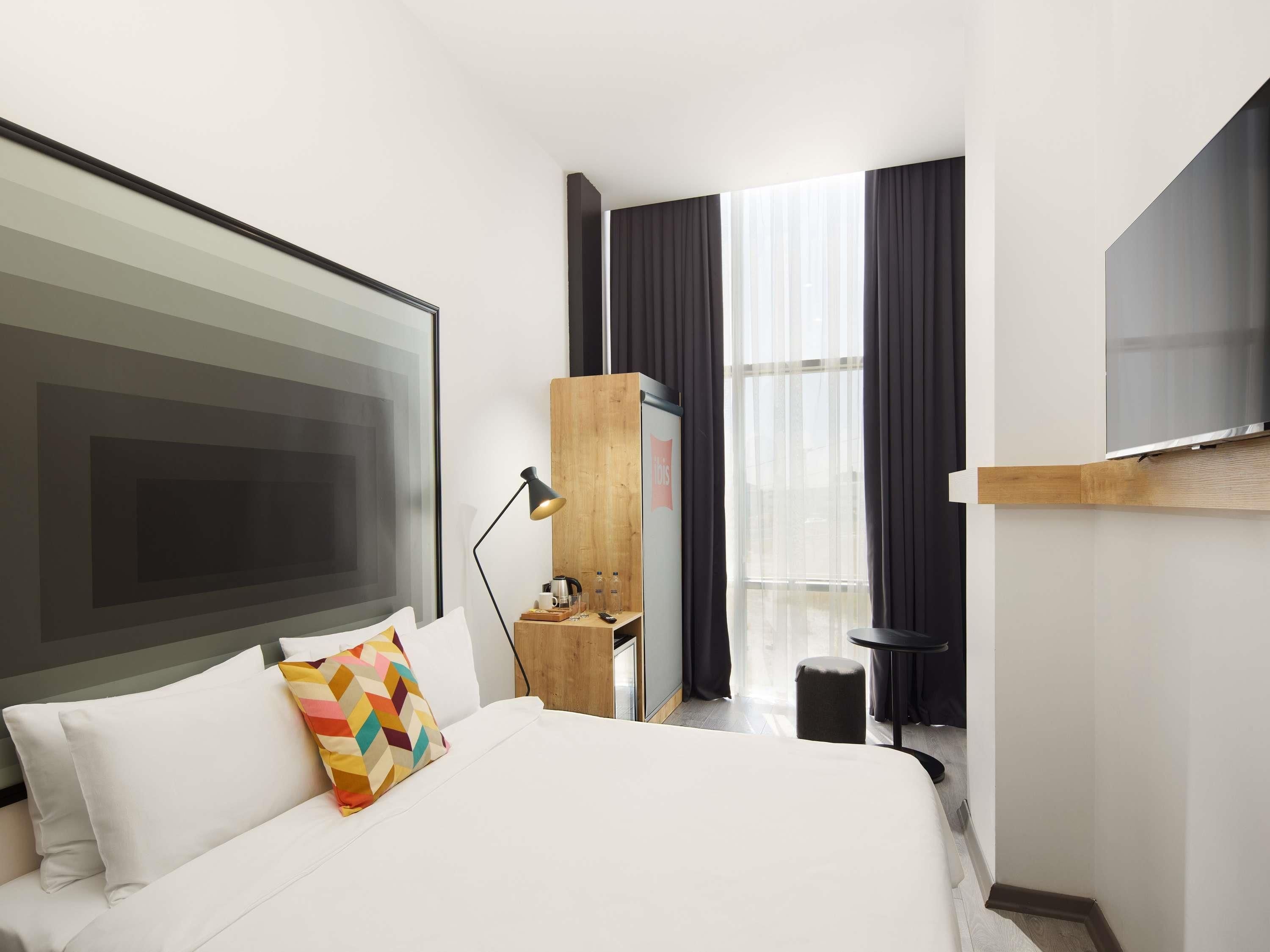 A modern hotel room with a large bed, a desk, a TV, and a window with curtains.