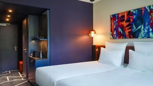 A hotel room with a bed, a nightstand, a painting, and a door leading to a bathroom.