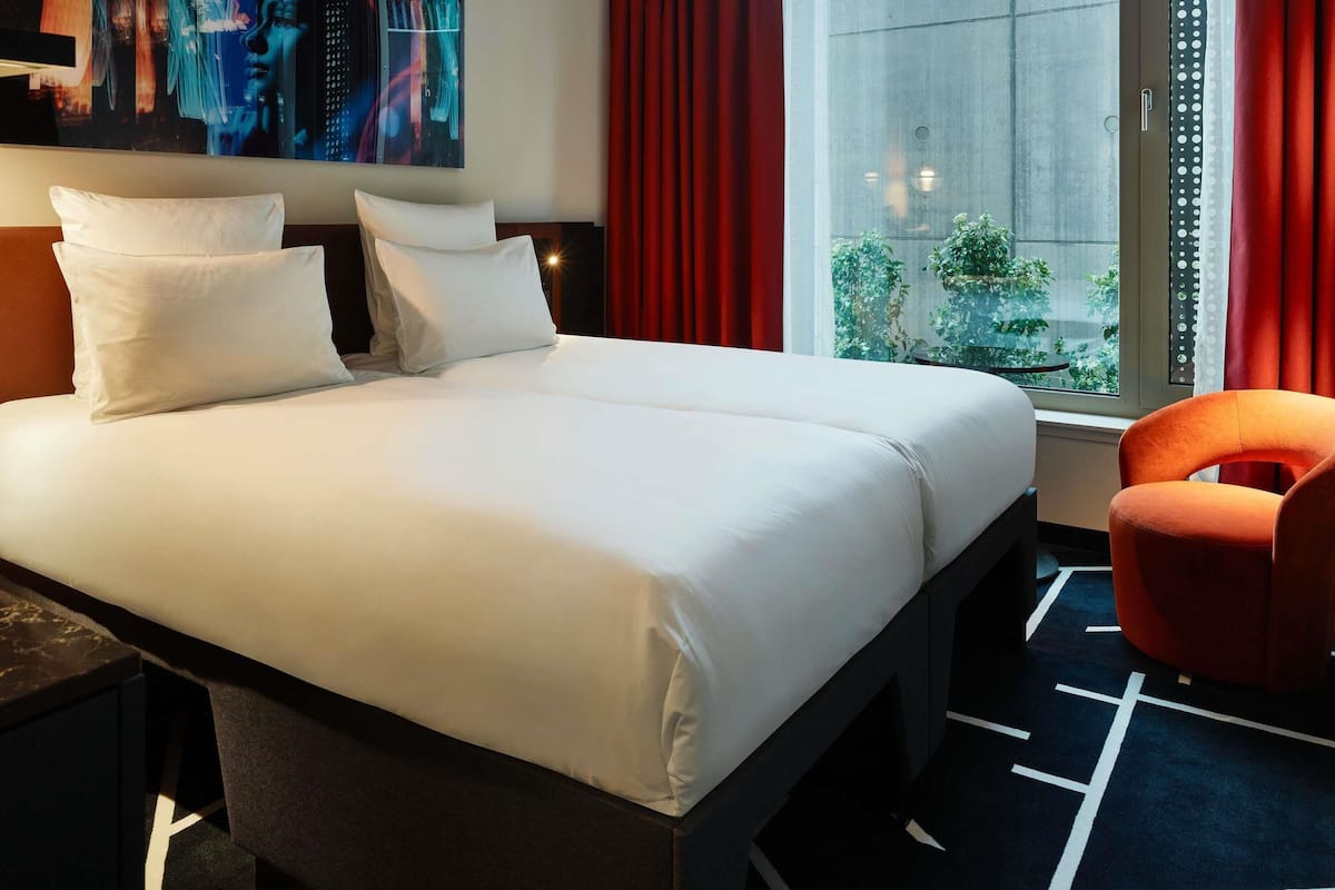 Ein Hotelzimmer mit einem Bett, einem Sessel, einem Bild an der Wand und einem Fenster mit Vorhängen.