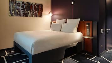 Relax in a stylish room with a large bed, abstract art, and a bedside table with a lamp.