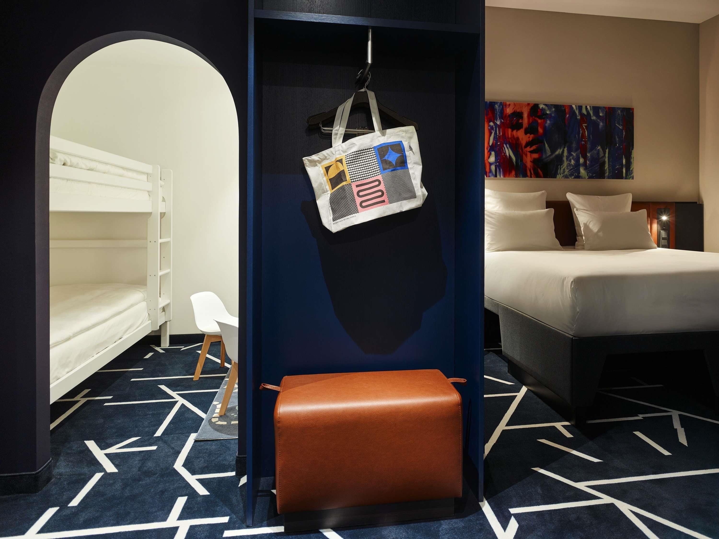 Habitación de hotel con literas, un escritorio con silla, un pequeño rincón de descanso y un cuadro en la pared.