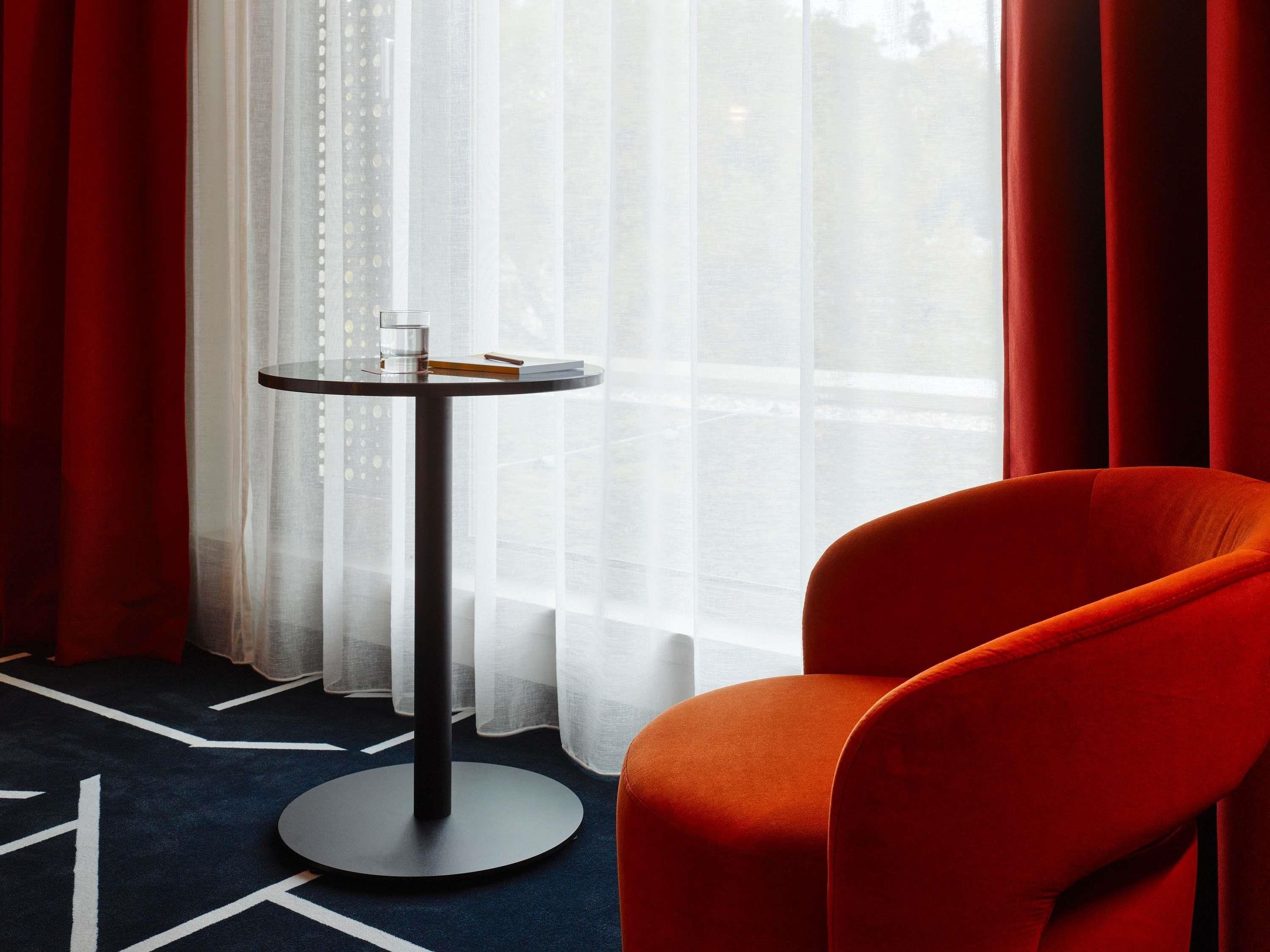 A room with a round table, a chair, and a view through sheer curtains.