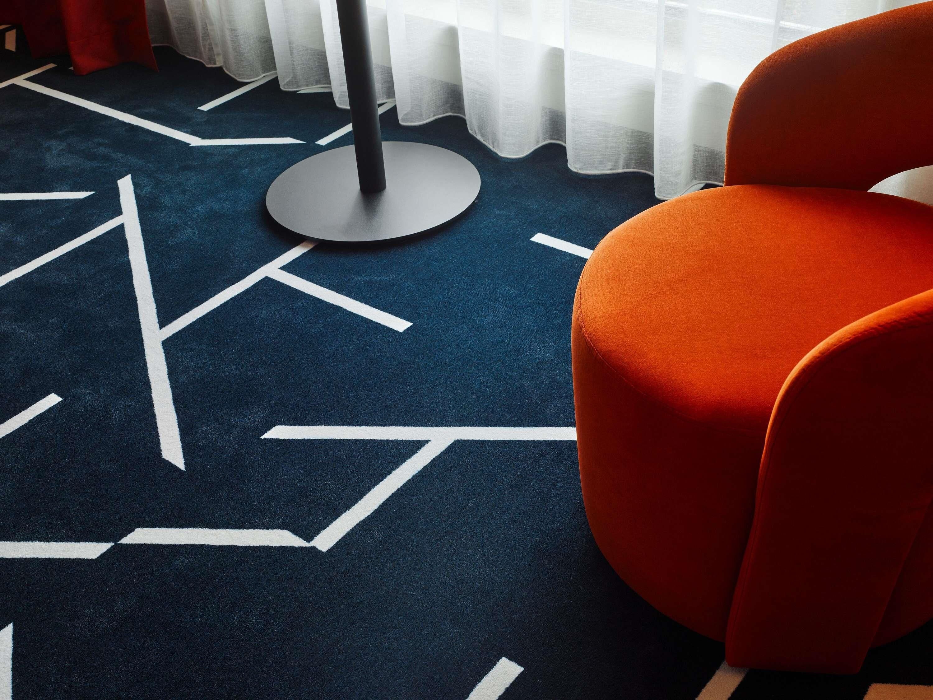 A room with a blue carpet featuring white geometric patterns, a round black table, and an orange chair.