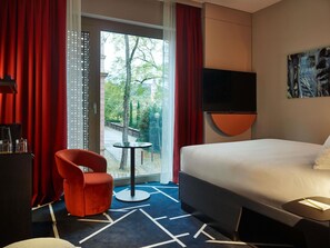 Une chambre d’hôtel avec un lit, une chaise rouge, une petite table, un téléviseur et une vue sur l’extérieur.