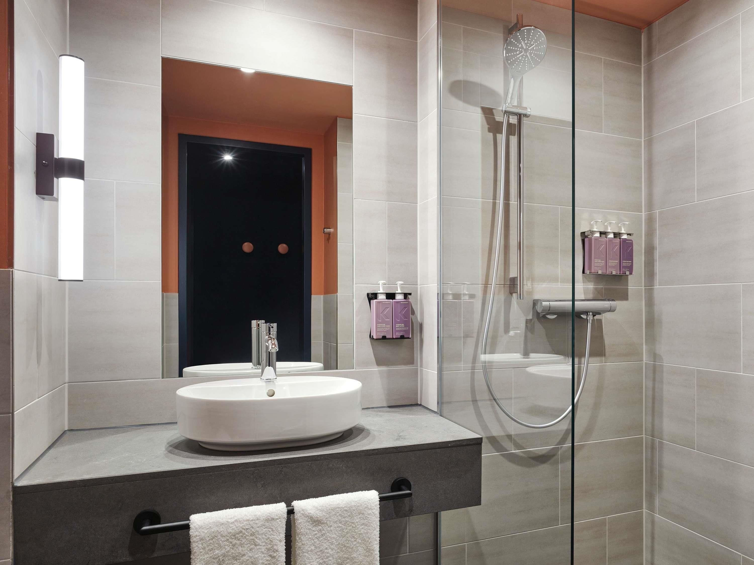 Un baño moderno con un lavamanos redondo, ducha con mampara de cristal y tocador con toallero.