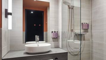 Un baño moderno con un lavamanos redondo, ducha con mampara de cristal y tocador con toallero.
