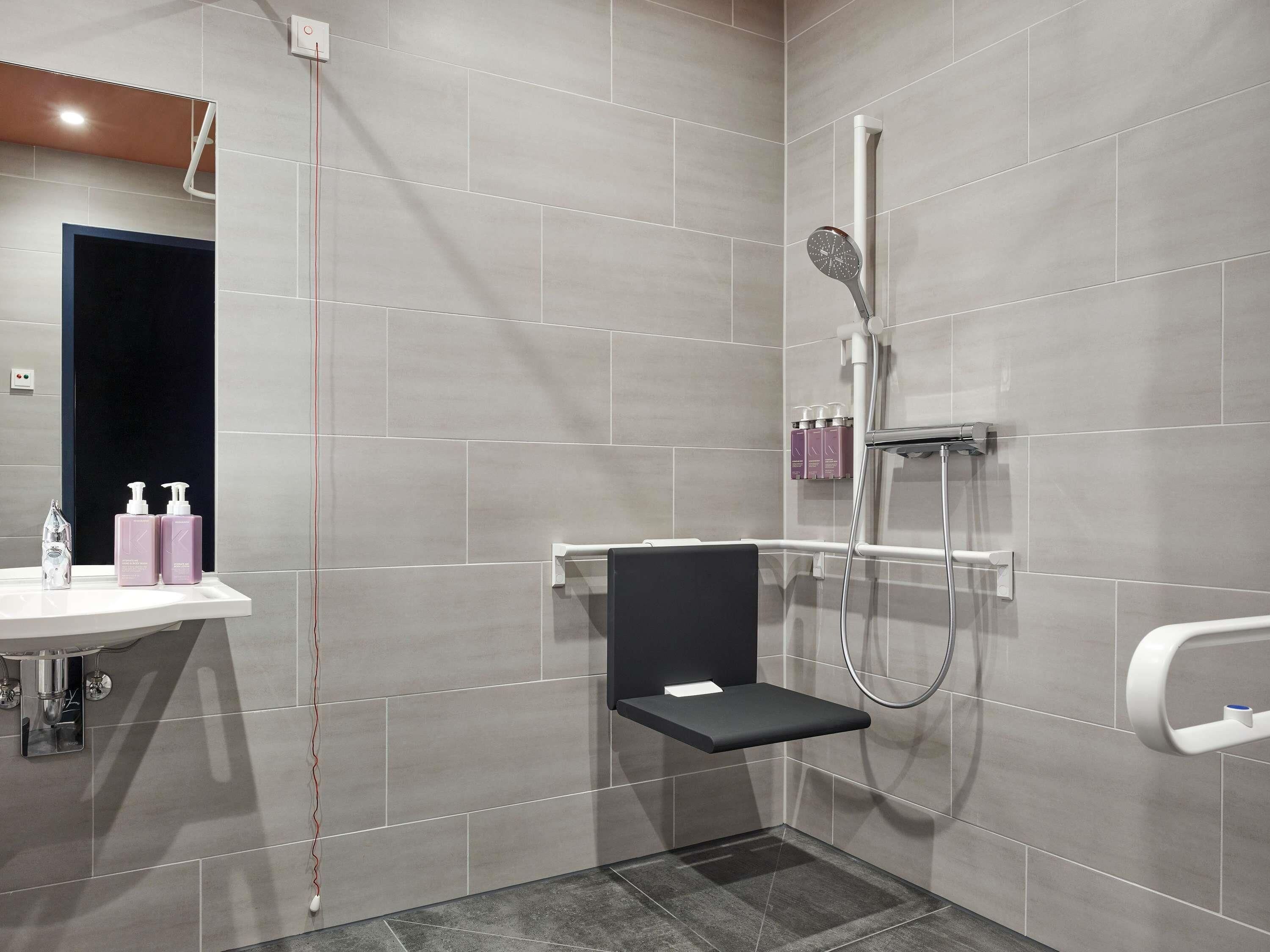 Ein modernes Badezimmer mit grauen Fliesen, einer Dusche, einem schwarzen Regal und einem weißen Waschbecken.