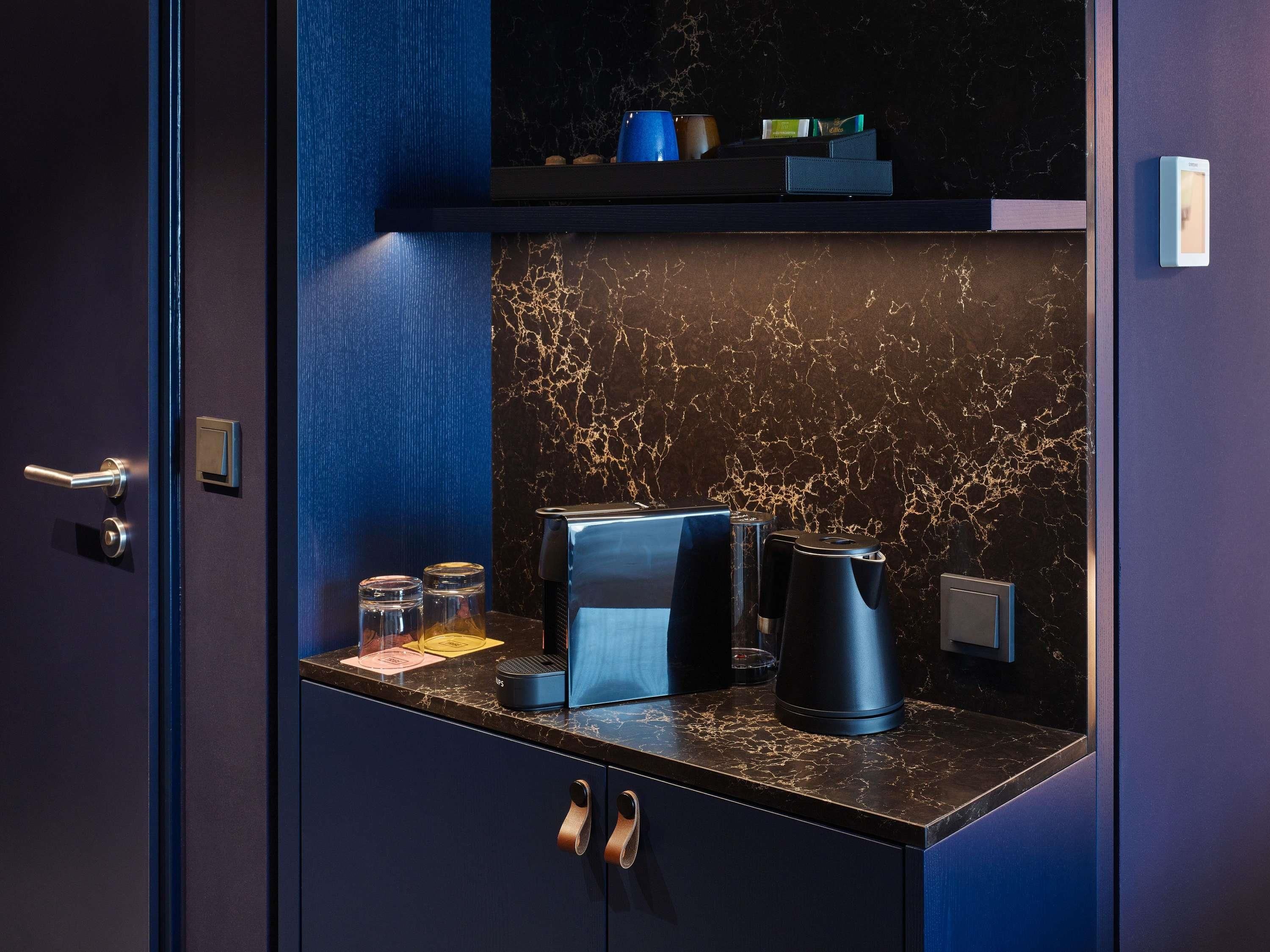 Eine moderne Küche mit Marmor-Spritzschutz, einer Kaffeemaschine, einem Wasserkocher und einem kleinen Regal mit Gegenständen.
