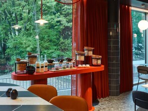 A modern interior with a dining area, a red accent wall, and a view of greenery outside. - TRIBE Baden-Baden (Baden-Baden)
