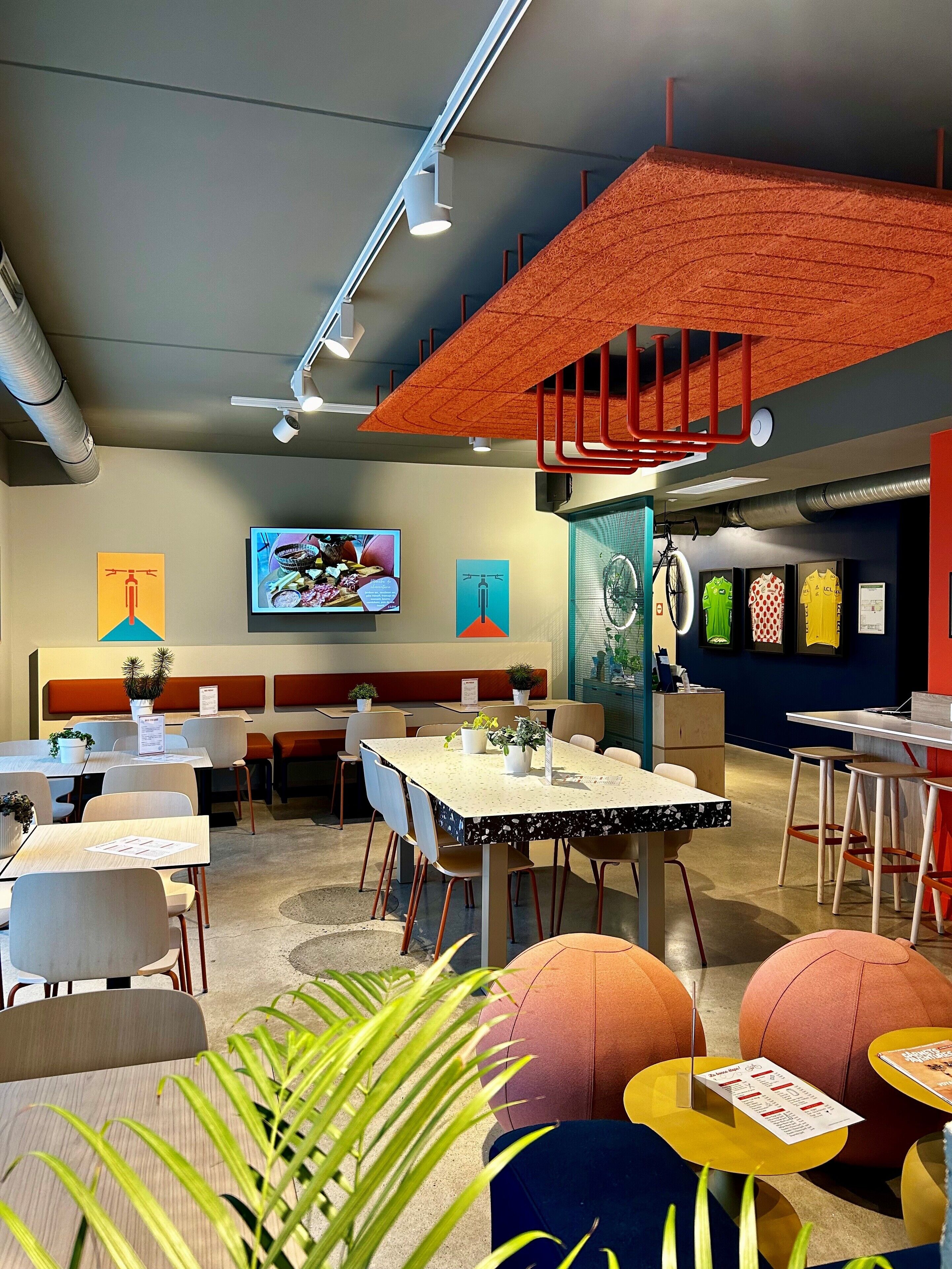 A modern indoor space with tables and chairs, a television screen, and various wall decorations.