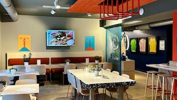 Un espacio interior moderno con mesas, sillas, una pantalla de televisión y diversas decoraciones en las paredes.