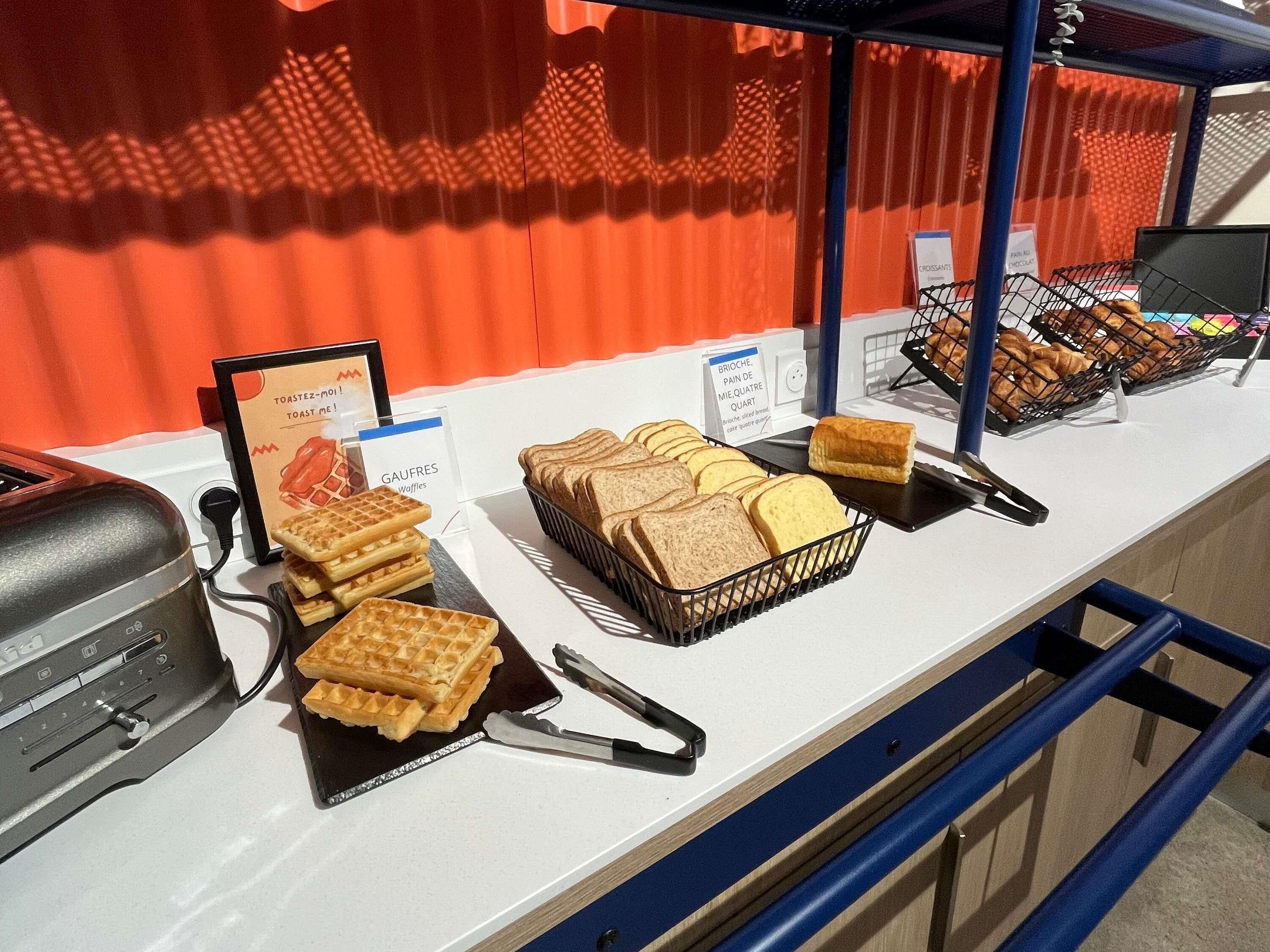 Een ontbijtbuffet met wafels, brood en croissants.