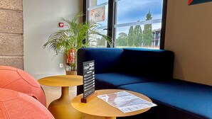 A modern lounge area with a blue sofa, two round tables with yellow bases, and a potted plant.