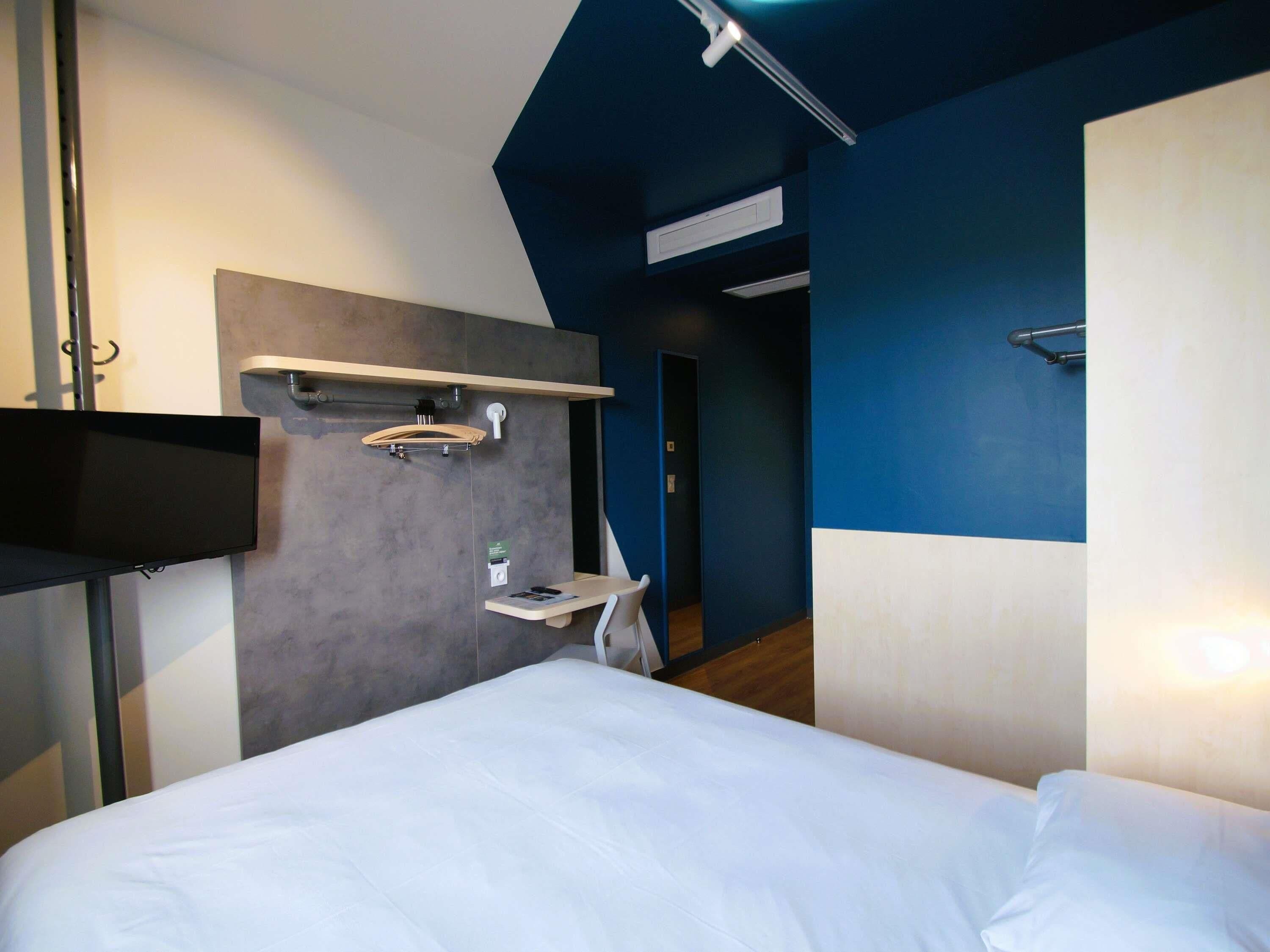 Una camera d'albergo con un letto, una scrivania, uno specchio e uno scaffale con un asciugamano.