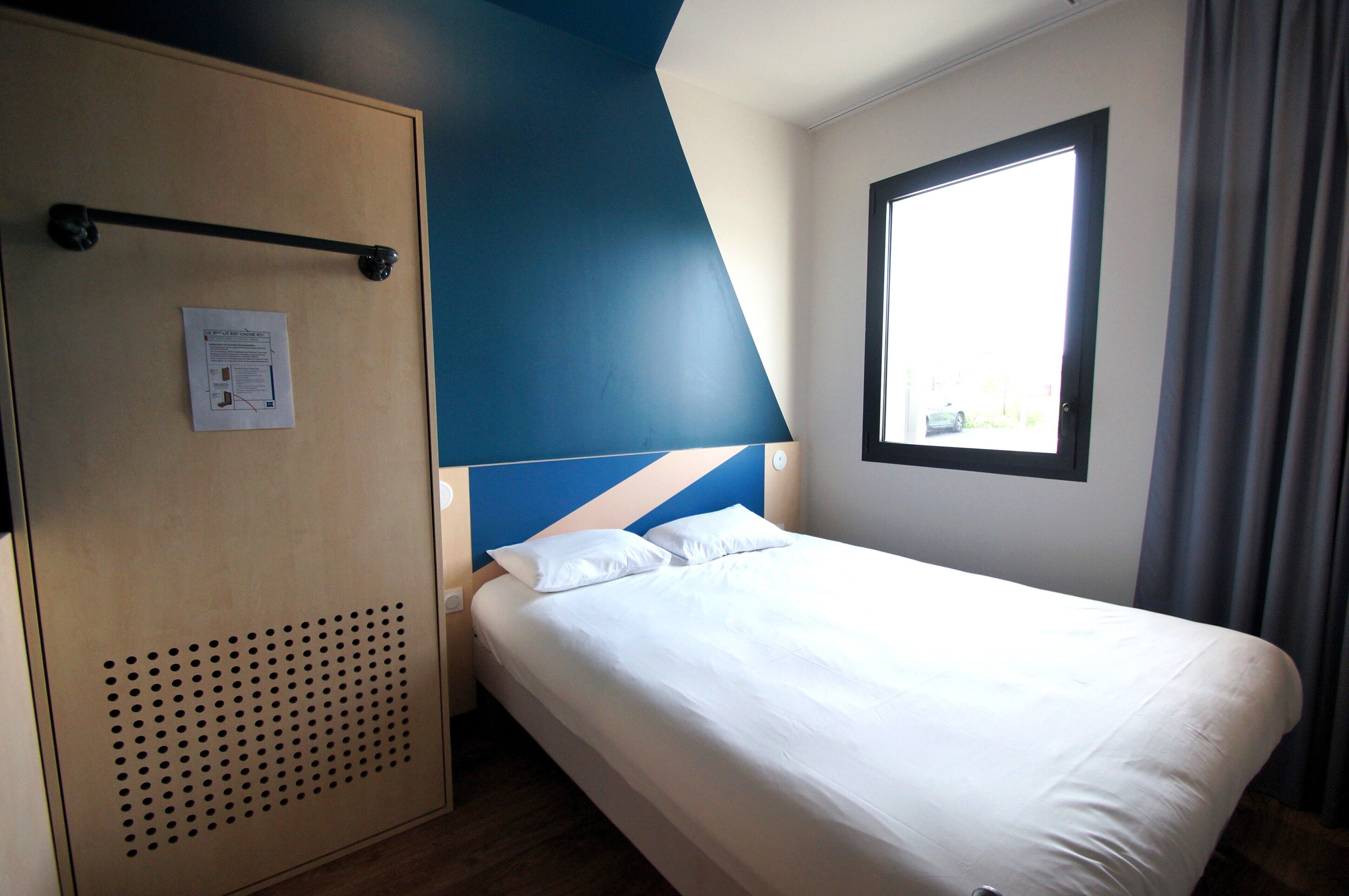 A hotel room with a bed, a wardrobe, a window, and a door with a vent.