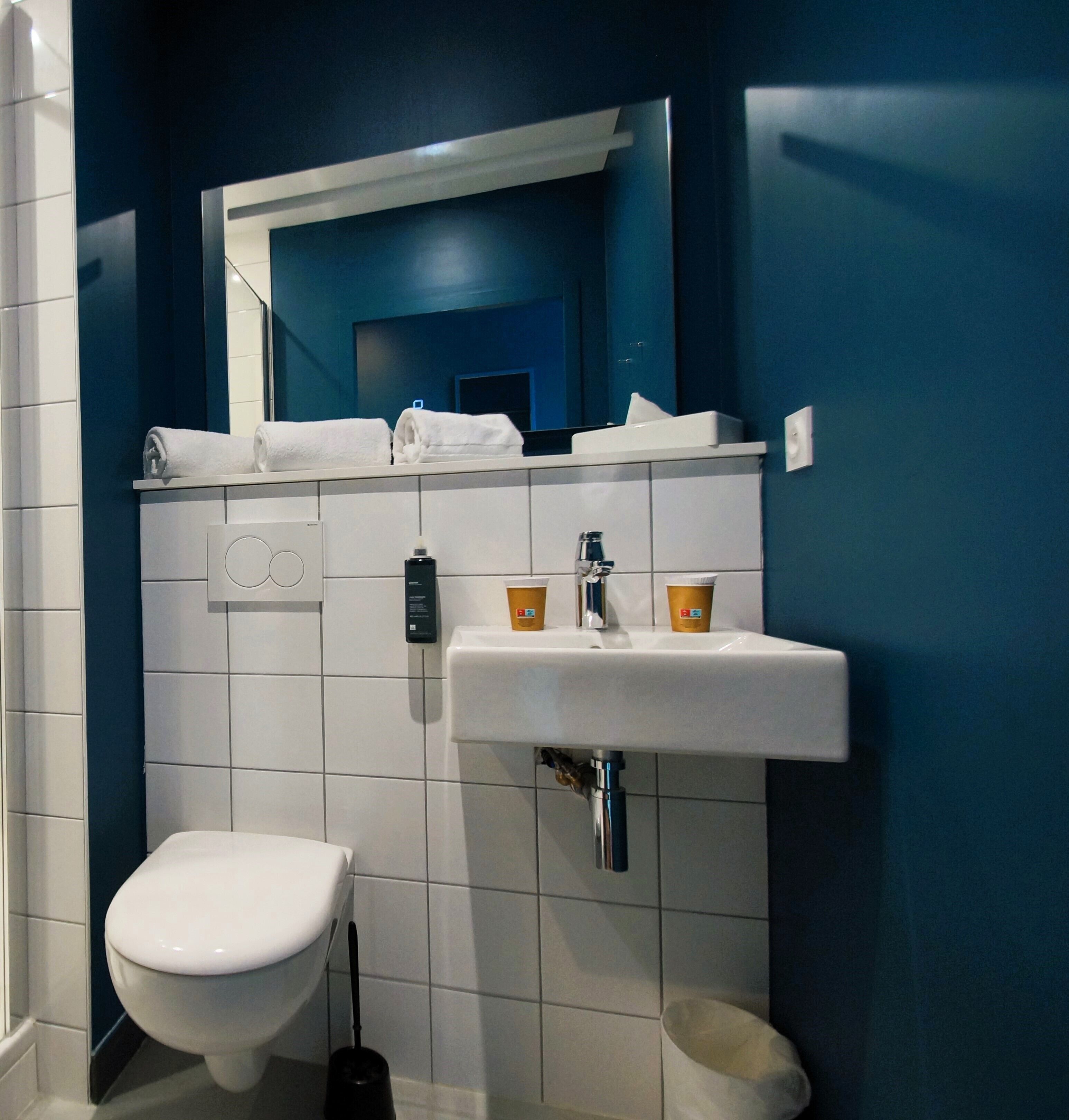 Un baño con inodoro blanco, lavabo con espejo y pared azul.