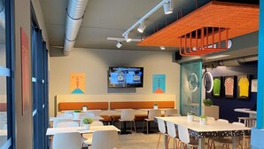 A modern dining area with tables, chairs, and a television screen.