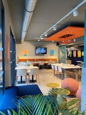 A modern dining area with tables, chairs, and a television screen. - Ibis Budget Loudéac Vélodrome (Ouverture Juillet 2023) (Loudeac)