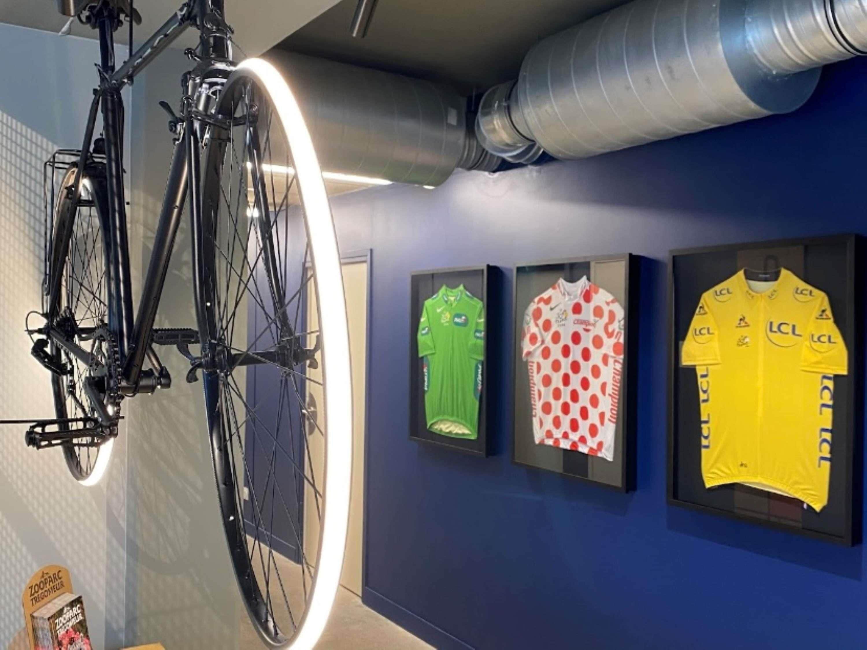 Een fiets aan een muur bevestigd, met daaronder drie shirts.