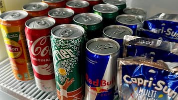 Un refrigerador lleno de diversas bebidas, incluyendo latas de refresco y un paquete de Capri-Sun.
