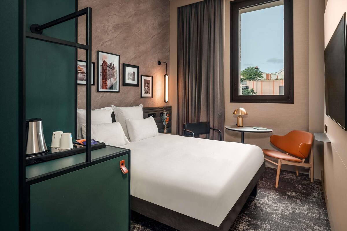 Une chambre d’hôtel équipée d’un lit, d’un bureau, d’une chaise, d’une télévision et d’une fenêtre donnant sur un paysage agréable.