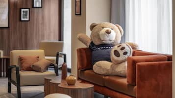 Un oso de peluche sobre un sofá marrón en un vestíbulo moderno con una pared de madera, una silla, una mesita y cuadros enmarcados.