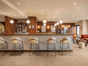 A bar area with a counter, bar stools, and a selection of bottles. - Novotel Orléans Centre Gare (Orléans)