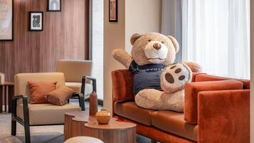A plush bear sitting on a sofa in a modern lounge area with a wooden wall and framed artwork.
