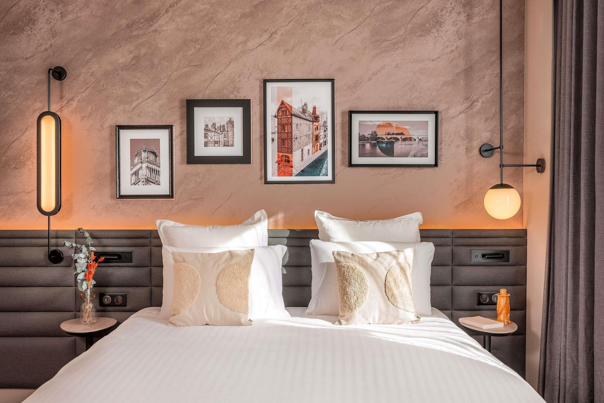 Ein Hotelzimmer mit einem Bett, zwei Nachttischen, einer Wandlampe und gerahmten Bildern.