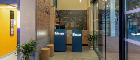 A reception area with a chalkboard displaying 'VALENCIA!' and two 'ibis budget' counters.