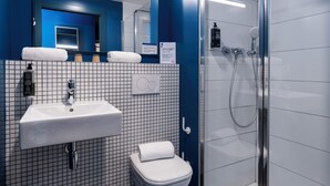 A bathroom with a white sink, a toilet, and a glass-enclosed shower. - Ibis Budget Valencia Centro Puerto (Valencia)