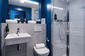 A bathroom with a white sink, a toilet, and a glass-enclosed shower. - Ibis Budget Valencia Centro Puerto (Valencia)