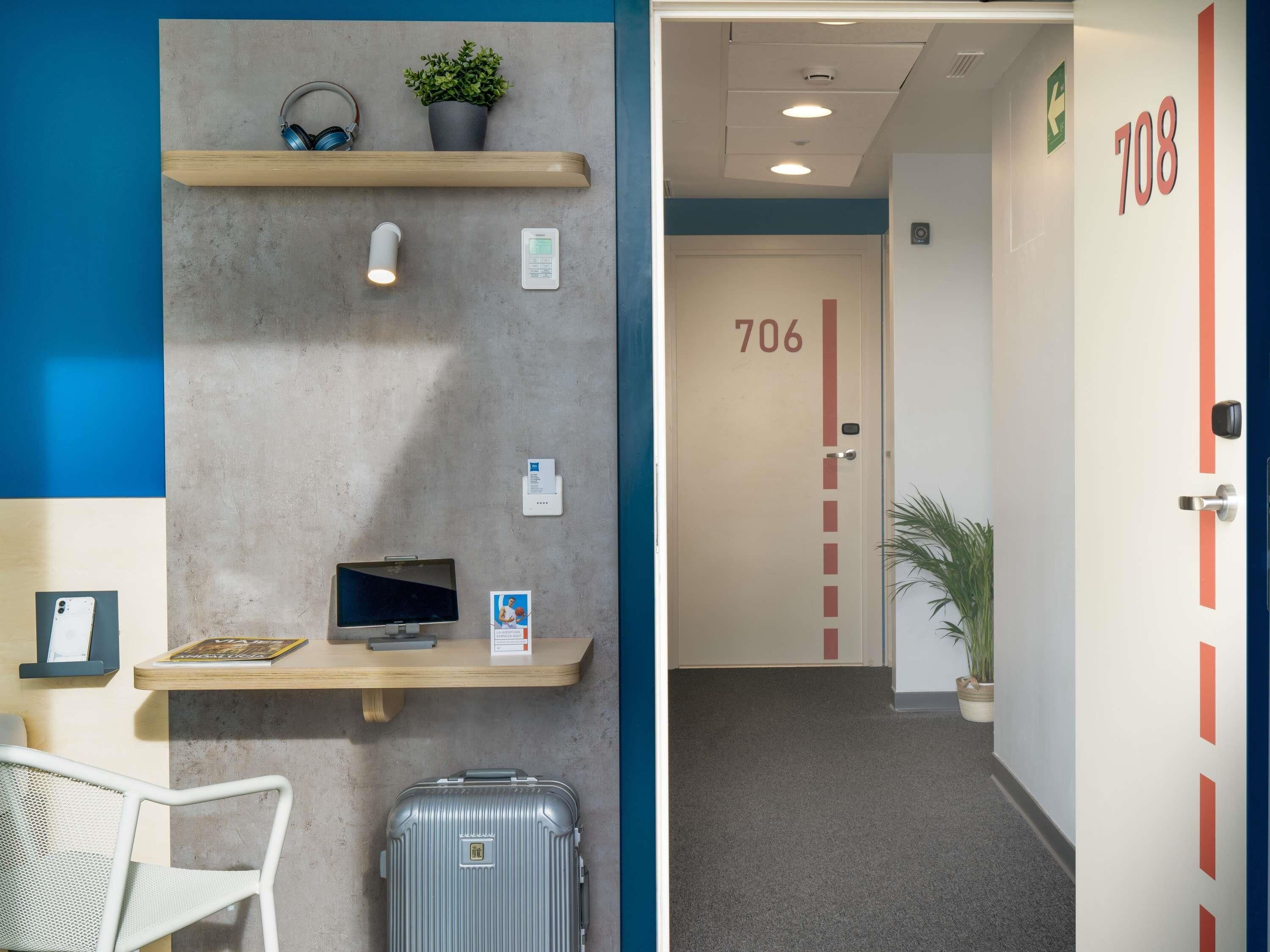 Un espace d’accueil d’hôtel comprenant un comptoir, une chaise, une plante, un thermostat fixé au mur et une porte portant le numéro 706.