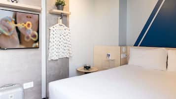 Quarto de hotel moderno com uma cama grande, uma televisão fixada na parede, uma pequena mesa com uma câmera e um cabide.