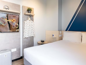 A modern hotel room with a large bed, a TV mounted on the wall, a small table with a camera, and a hanging garment. - Ibis Budget Valencia Centro Puerto (Valencia)