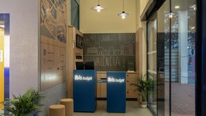 A reception area with two blue 'ibis budget' counters, a chalkboard with drawings, and a large window. - Ibis Budget Valencia Centro Puerto (Valencia)