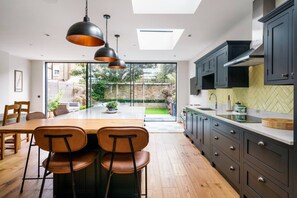 A modern kitchen with dark cabinets, a wooden dining table, and two chairs. - Enjoy 4 floors of modern luxury nr River Thames (London)