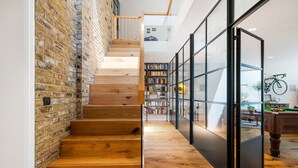 A wooden staircase with a brick wall on one side, leading to a room with a bookshelf and a billiards table.