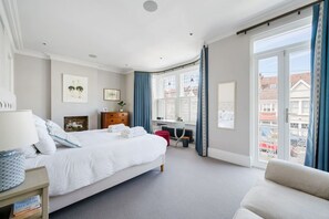 A bedroom with a bed, a desk, a chair, a radiator, and a window with a view of buildings. - Enjoy 4 floors of modern luxury nr River Thames (London)