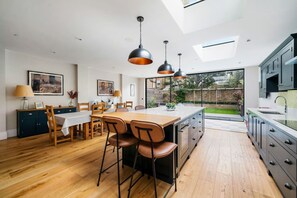 A modern kitchen with a dining area, featuring a large island, pendant lighting, and a view of the backyard.